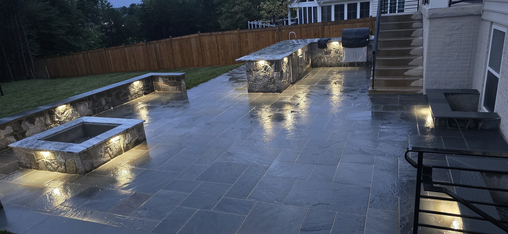 Completed illuminated stone patio with sitting walls, fire feature, and outdoor kitchen